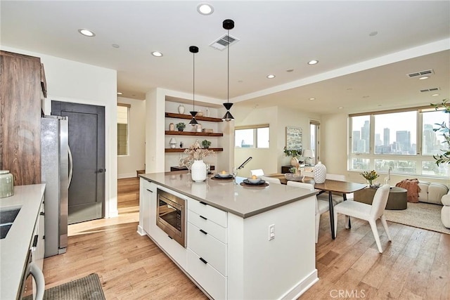 kitchen featuring a center island, stainless steel appliances, pendant lighting, white cabinets, and light wood-type flooring