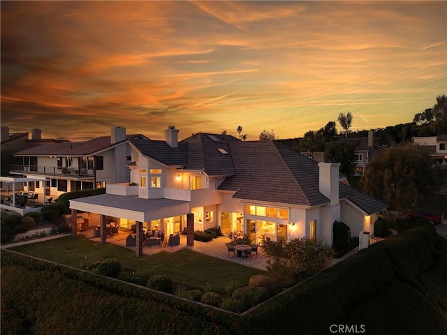 back house at dusk featuring a lawn, a patio area, and a balcony