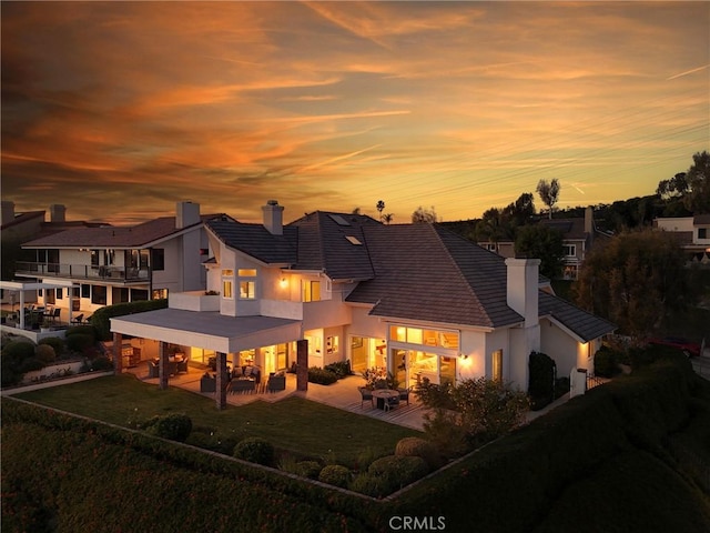 back house at dusk featuring a lawn, a patio area, and a balcony