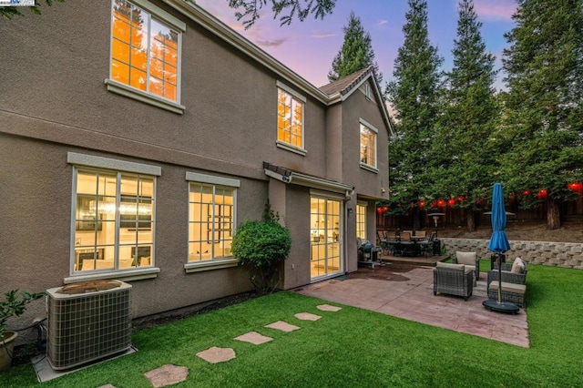 back house at dusk featuring an outdoor hangout area, central air condition unit, a yard, and a patio