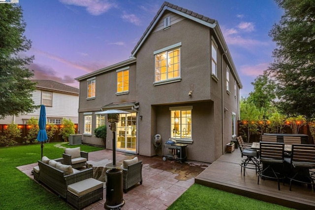 back house at dusk with a deck, an outdoor living space, and a lawn