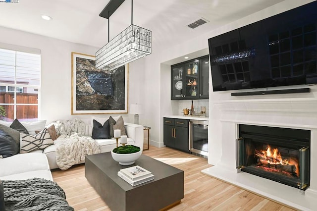 living room with bar area, beverage cooler, an inviting chandelier, and light wood-type flooring