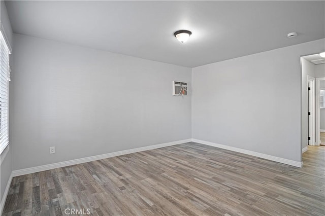 spare room featuring wood-type flooring, an AC wall unit, and a healthy amount of sunlight