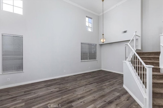 unfurnished living room featuring crown molding, a towering ceiling, and dark wood-type flooring