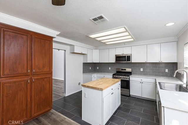 kitchen with sink, dark tile patterned floors, appliances with stainless steel finishes, a kitchen island, and white cabinetry