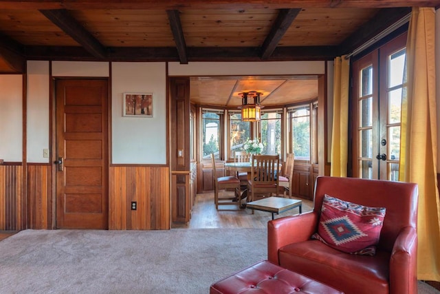 sitting room featuring beam ceiling, french doors, wooden ceiling, and wood walls