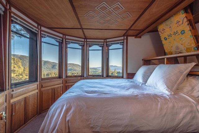 bedroom featuring carpet flooring, a mountain view, wooden ceiling, and multiple windows