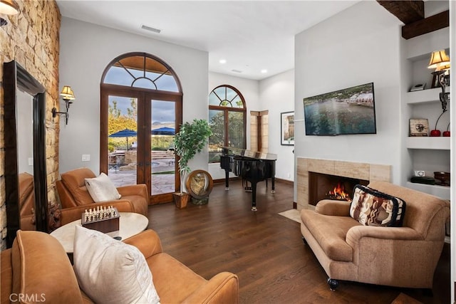 living room featuring a tile fireplace, dark hardwood / wood-style floors, built in features, and french doors