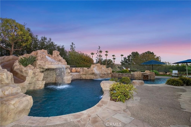 pool at dusk with pool water feature and a patio