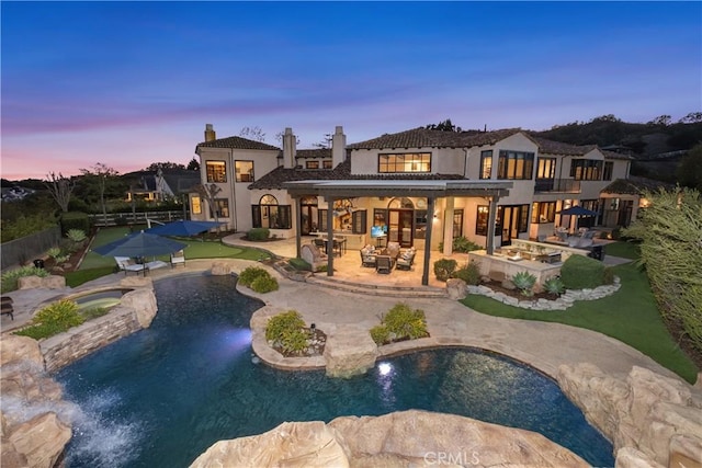 back house at dusk with a pool with hot tub and a patio