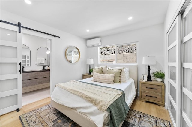 bedroom with a wall mounted air conditioner, a barn door, and wood-type flooring