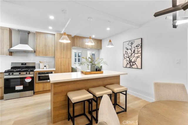 kitchen with decorative backsplash, appliances with stainless steel finishes, wall chimney exhaust hood, pendant lighting, and light brown cabinets