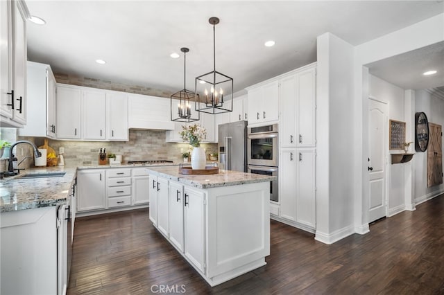 kitchen with a kitchen island, appliances with stainless steel finishes, pendant lighting, white cabinetry, and sink