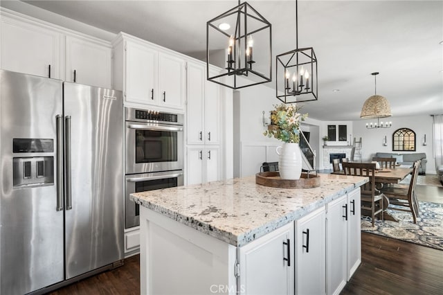 kitchen featuring appliances with stainless steel finishes, decorative light fixtures, white cabinetry, a center island, and light stone countertops