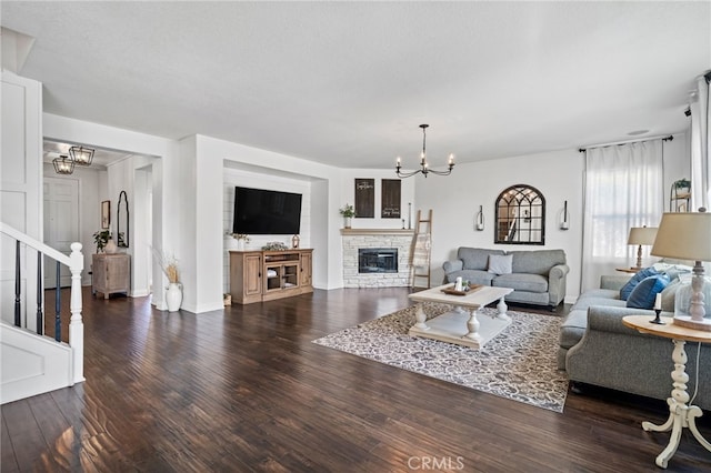 living room with a stone fireplace, dark wood-type flooring, a textured ceiling, and a chandelier