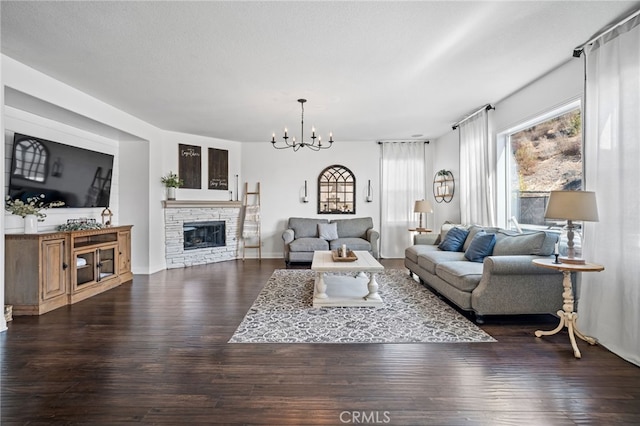 living room with dark wood-type flooring, a stone fireplace, a chandelier, and a textured ceiling