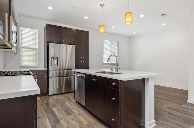 kitchen featuring appliances with stainless steel finishes, sink, decorative light fixtures, and a kitchen island with sink