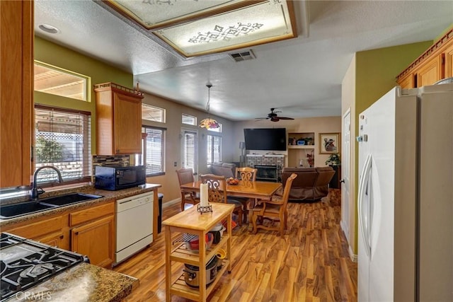 kitchen featuring a brick fireplace, white appliances, ceiling fan, sink, and light hardwood / wood-style floors