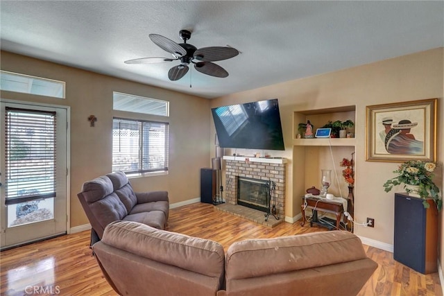 living room with ceiling fan, wood-type flooring, a textured ceiling, and a brick fireplace