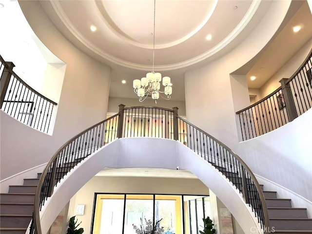 staircase with a tray ceiling, a notable chandelier, and a towering ceiling