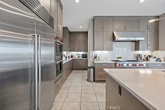 kitchen with light tile patterned floors, wall chimney range hood, appliances with stainless steel finishes, and tasteful backsplash