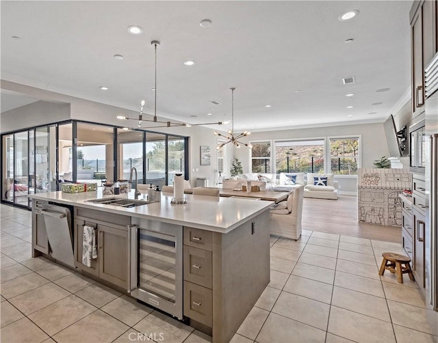 kitchen featuring beverage cooler, sink, hanging light fixtures, a notable chandelier, and a center island with sink