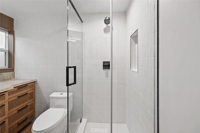 bathroom featuring vanity, toilet, a shower with shower door, and tile walls