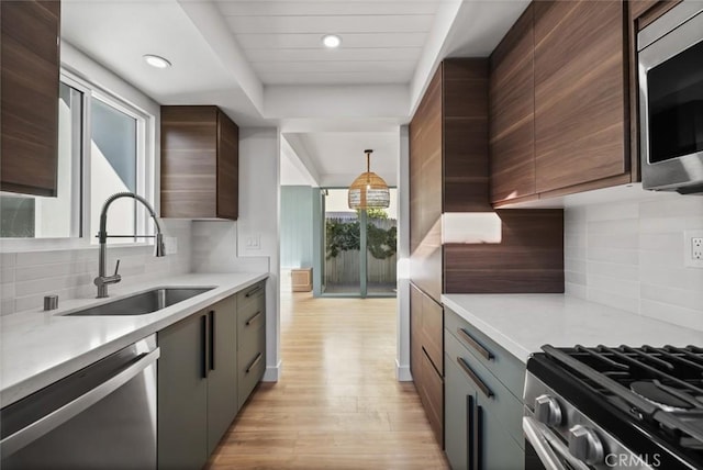 kitchen with appliances with stainless steel finishes, light wood-type flooring, tasteful backsplash, sink, and pendant lighting