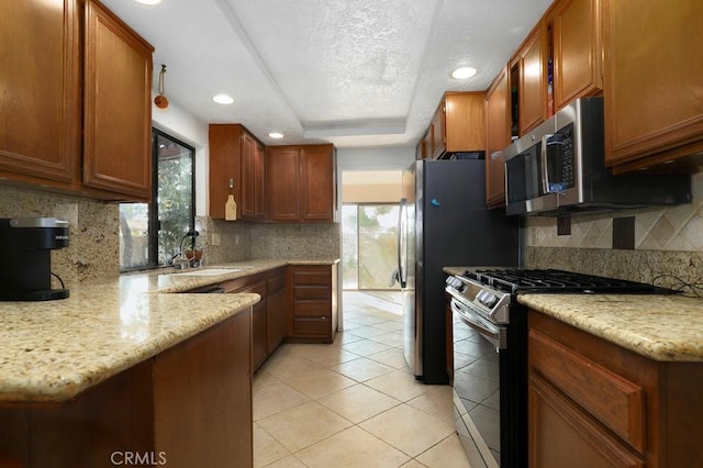 kitchen with sink, stainless steel appliances, tasteful backsplash, light stone counters, and light tile patterned floors