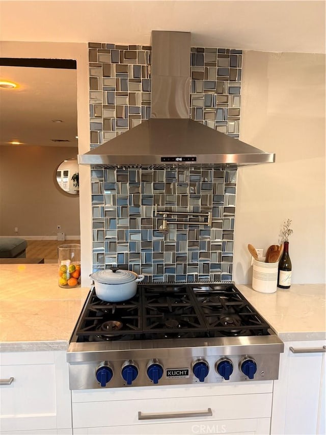 kitchen with stainless steel gas stovetop, white cabinetry, wall chimney range hood, and backsplash