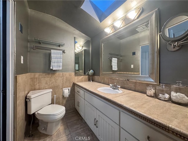 bathroom with lofted ceiling with skylight, tile walls, tile patterned flooring, vanity, and toilet