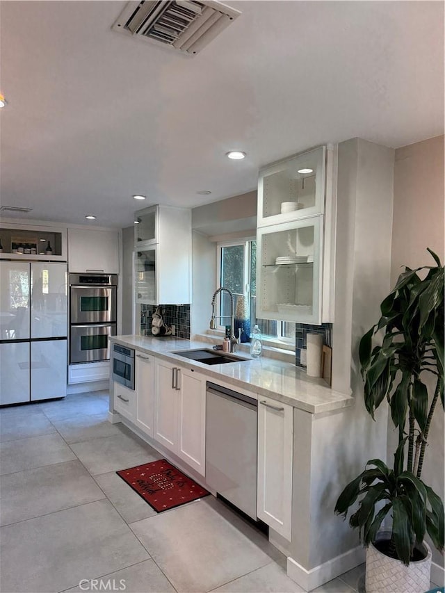 kitchen with tasteful backsplash, white cabinetry, sink, light tile patterned floors, and stainless steel appliances