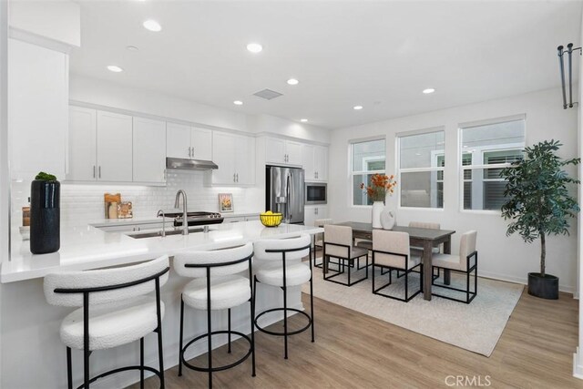 kitchen with light hardwood / wood-style flooring, white cabinetry, stainless steel appliances, and kitchen peninsula