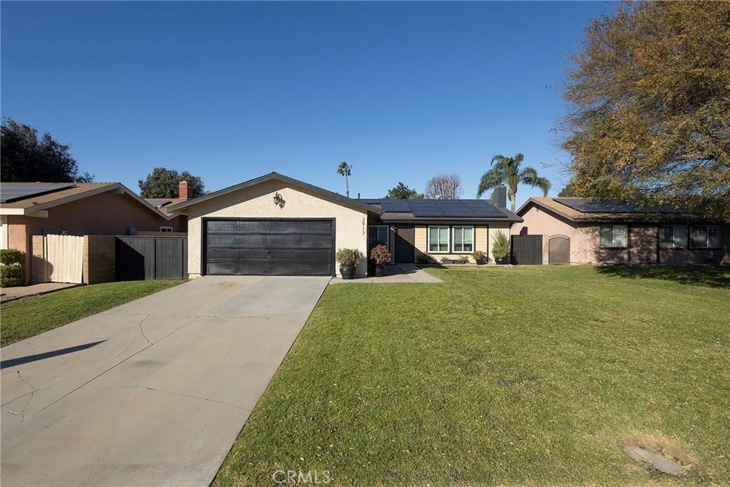 ranch-style house featuring a front lawn, a garage, and solar panels