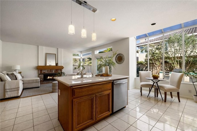 kitchen featuring a center island with sink, a fireplace, pendant lighting, stainless steel dishwasher, and sink