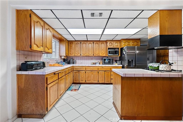 kitchen with island exhaust hood, appliances with stainless steel finishes, tile countertops, and tasteful backsplash