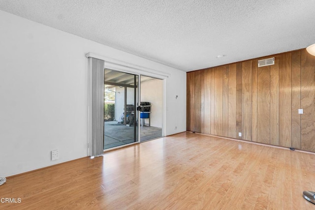 unfurnished room with a textured ceiling, light hardwood / wood-style floors, and wooden walls