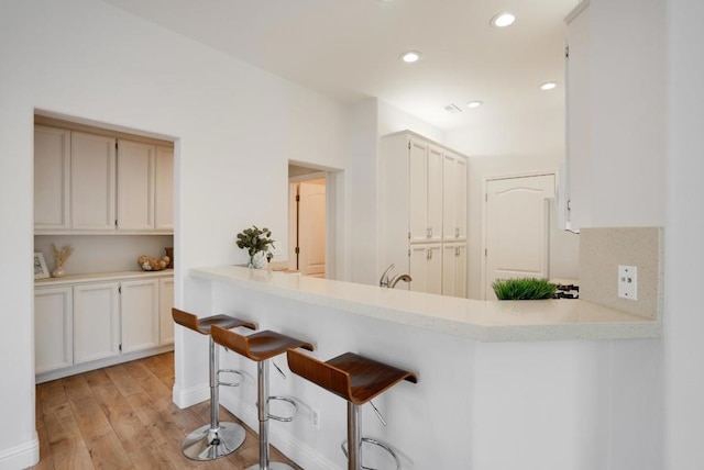 kitchen with kitchen peninsula, light wood-type flooring, white cabinets, a breakfast bar, and sink