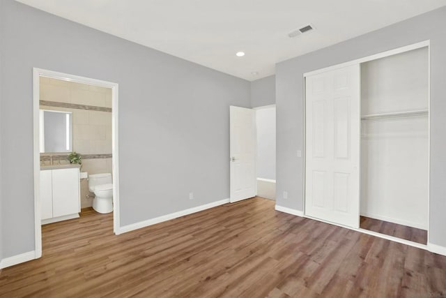 unfurnished bedroom featuring ensuite bathroom, sink, hardwood / wood-style floors, and a closet