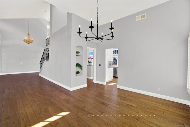 unfurnished living room featuring built in shelves, a towering ceiling, dark hardwood / wood-style floors, and an inviting chandelier