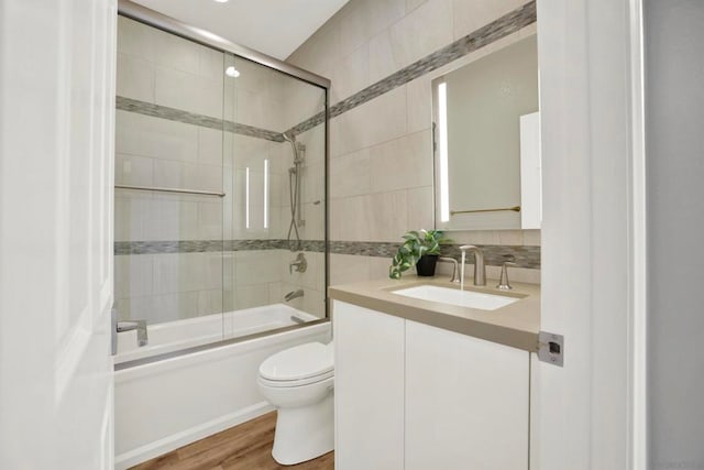 full bathroom with combined bath / shower with glass door, tasteful backsplash, hardwood / wood-style flooring, vanity, and toilet