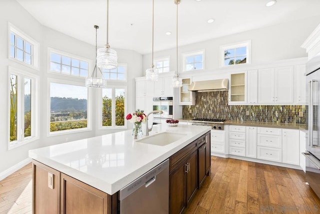 kitchen with sink, appliances with stainless steel finishes, white cabinetry, hanging light fixtures, and an island with sink