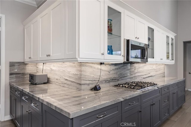 kitchen with crown molding, white cabinetry, light wood-type flooring, light stone countertops, and stainless steel appliances