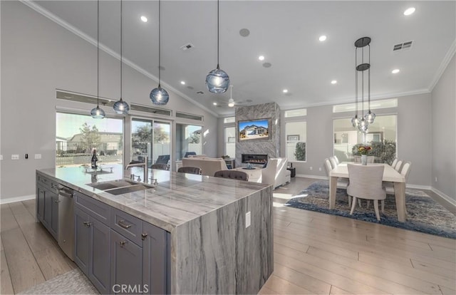 kitchen featuring light stone countertops, dishwasher, decorative light fixtures, an island with sink, and sink