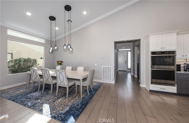 dining room with dark wood-type flooring, plenty of natural light, crown molding, and a towering ceiling