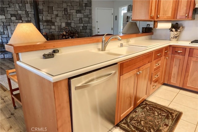 kitchen with dishwasher, a stone fireplace, sink, light tile patterned floors, and kitchen peninsula