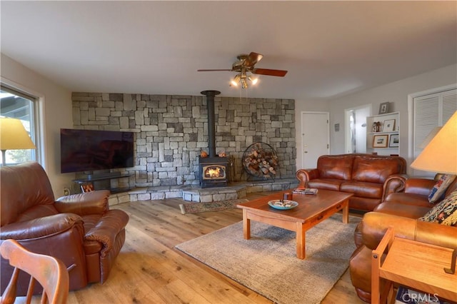 living room with a wood stove, ceiling fan, and light wood-type flooring