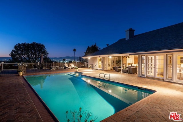 pool at dusk with french doors and a patio area