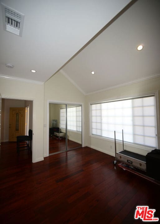 interior space featuring lofted ceiling, crown molding, and dark wood-type flooring