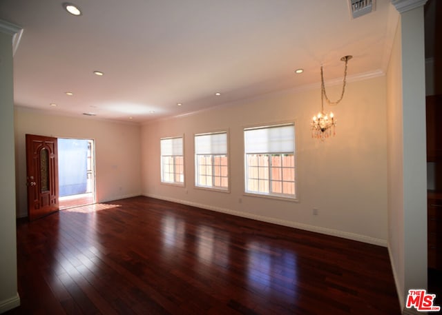 spare room featuring crown molding, dark wood-type flooring, and an inviting chandelier